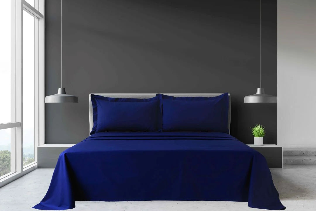 Navy blue King and Super King percale sheet set with flat sheet and matching pillowcases arranged on a large hotel bed.