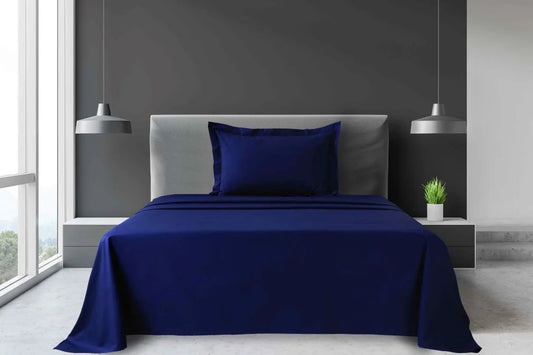Navy blue King and Super King percale sheet set with flat sheet and matching pillowcases arranged on a large hotel bed.