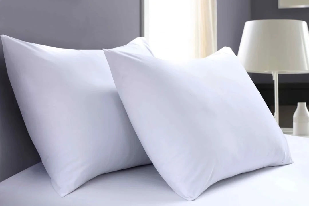 Close-up of two white percale pillowcases with a white fitted sheet on a hotel-style bed.