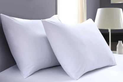 Close-up of two white percale pillowcases with a white fitted sheet on a hotel-style bed.